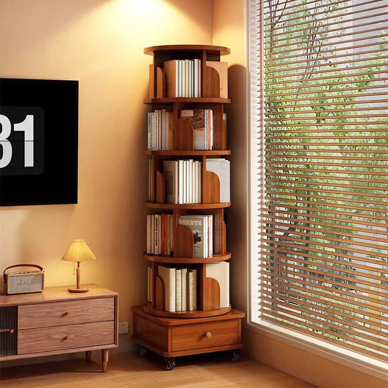 A tall, narrow wooden corner bookshelf with multiple curved shelves holding books, placed in a sunlit room next to a window with blinds and a small side table.