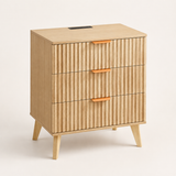 A mid-century modern wooden nightstand with three vertically fluted drawers, tapered legs, and orange handles, shown on a clean off-white background.