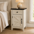 A rustic white nightstand with a black top and black hardware, styled next to a bed in a warm, neutral bedroom setting.