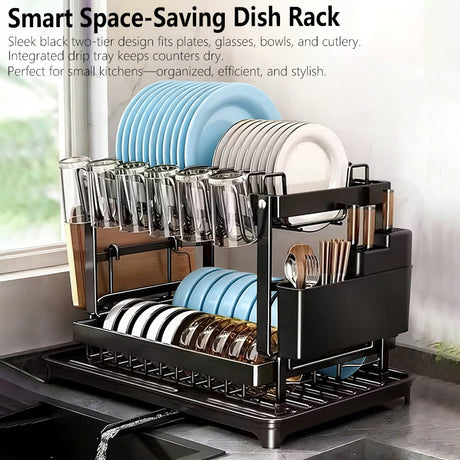 A black two-tier space-saving dish rack filled with plates, bowls, glasses, and cutlery, shown in a kitchen setting with text overlay at the top describing its features.