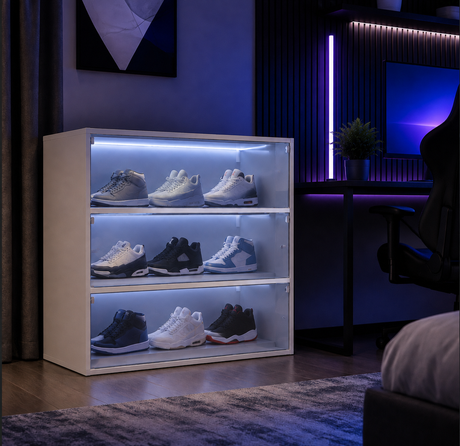 A three-tier sneaker display cabinet with LED lighting, filled with various sneakers, set in a modern gaming room environment.