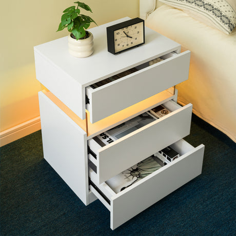 White nightstand with open drawer, clock, and plant in a bedroom setting