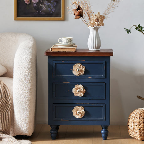 Blue nightstand with floral handles next to a beige armchair in a room.