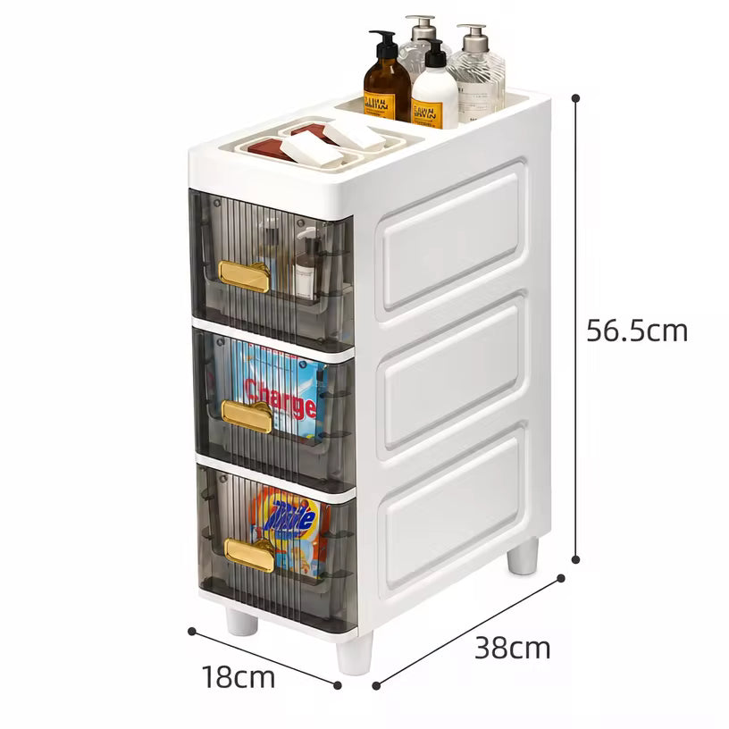 White plastic bathroom organizer cabinet with three transparent drawers and gold handles, shown with dimension labels 56.5cm, 38cm, and 18cm on a light gray background.
