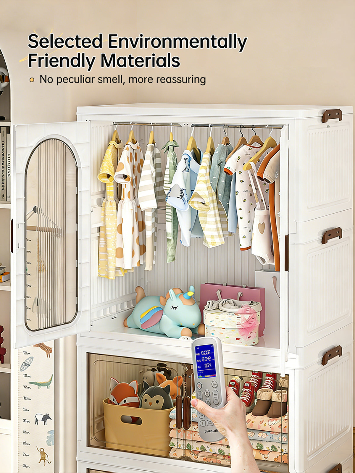 A white plastic baby storage closet with a glass door, shown open and filled with baby clothes, toys, and storage bins. A hand holding a remote control is visible in the foreground.